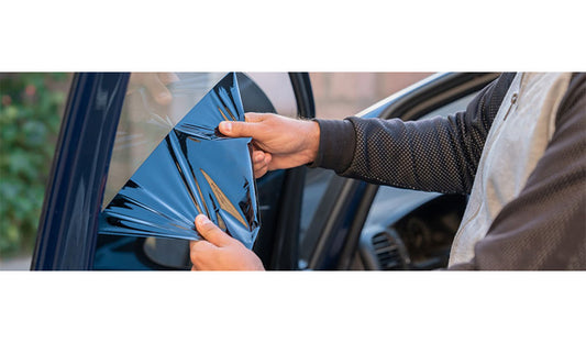 A man applying blue window tint to a car. Enhancing the vehicle's appearance and providing privacy.