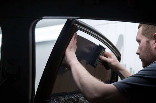 A man repairs a car window with tools focused beside the vehicle