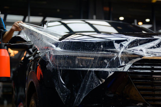 A man uses a sprayer to wash a car, ensuring it is clean and shiny under the sunlight