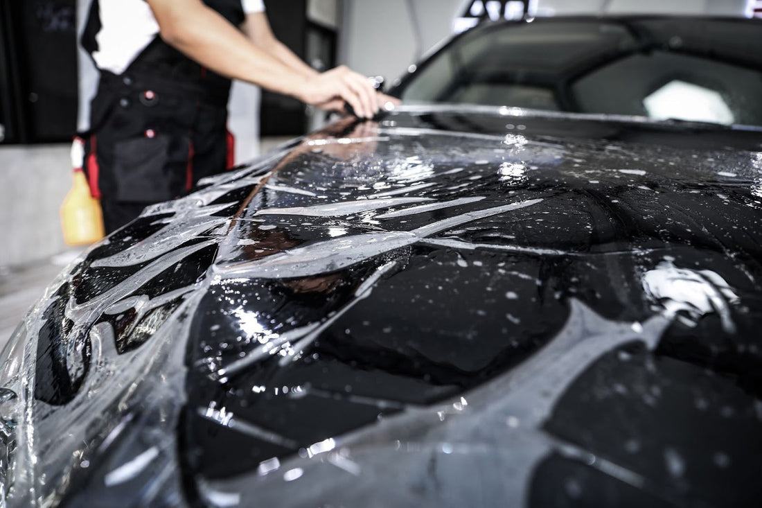 A person applying a protective film to a car's surface in a workshop.