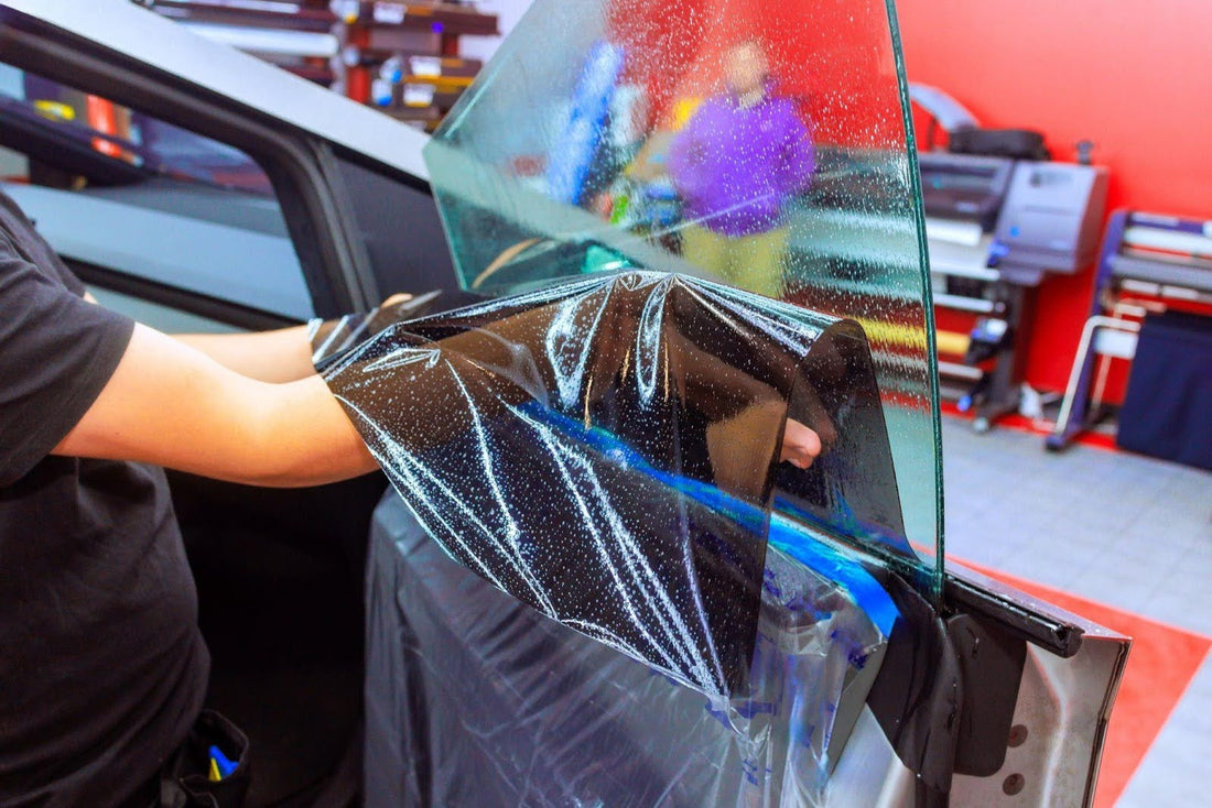 A person applying window tint to a car, carefully smoothing the film for a perfect finish