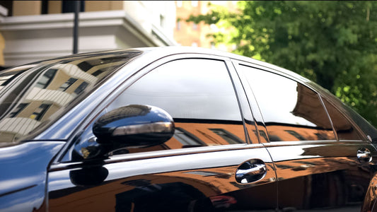 Close-up of a shiny black car reflecting buildings and trees.