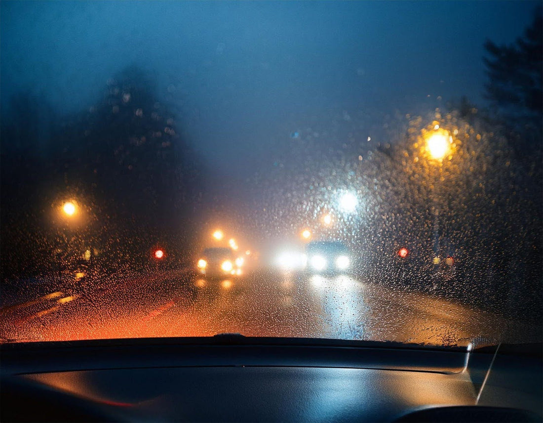 View from inside a car at night showcasing illuminated streetlights and distant city buildings through the windshield